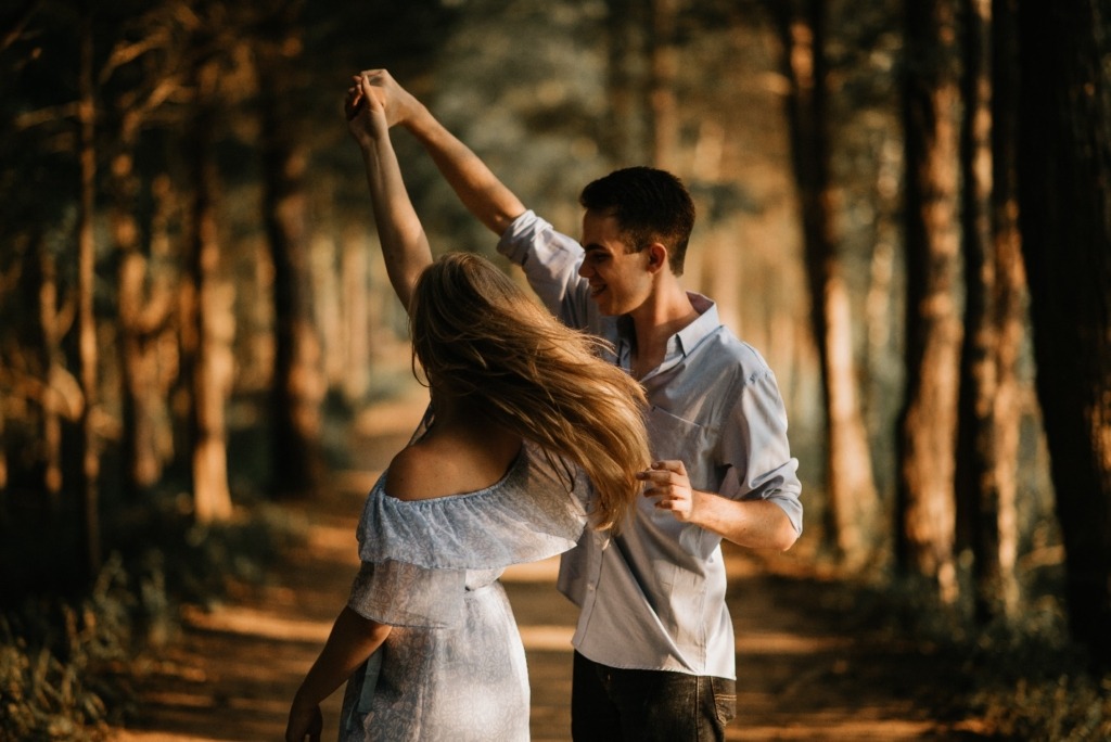 A young man spins a woman around in a forest
